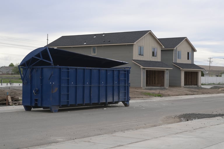 Large blue construction dumpster in front of new duplex homes