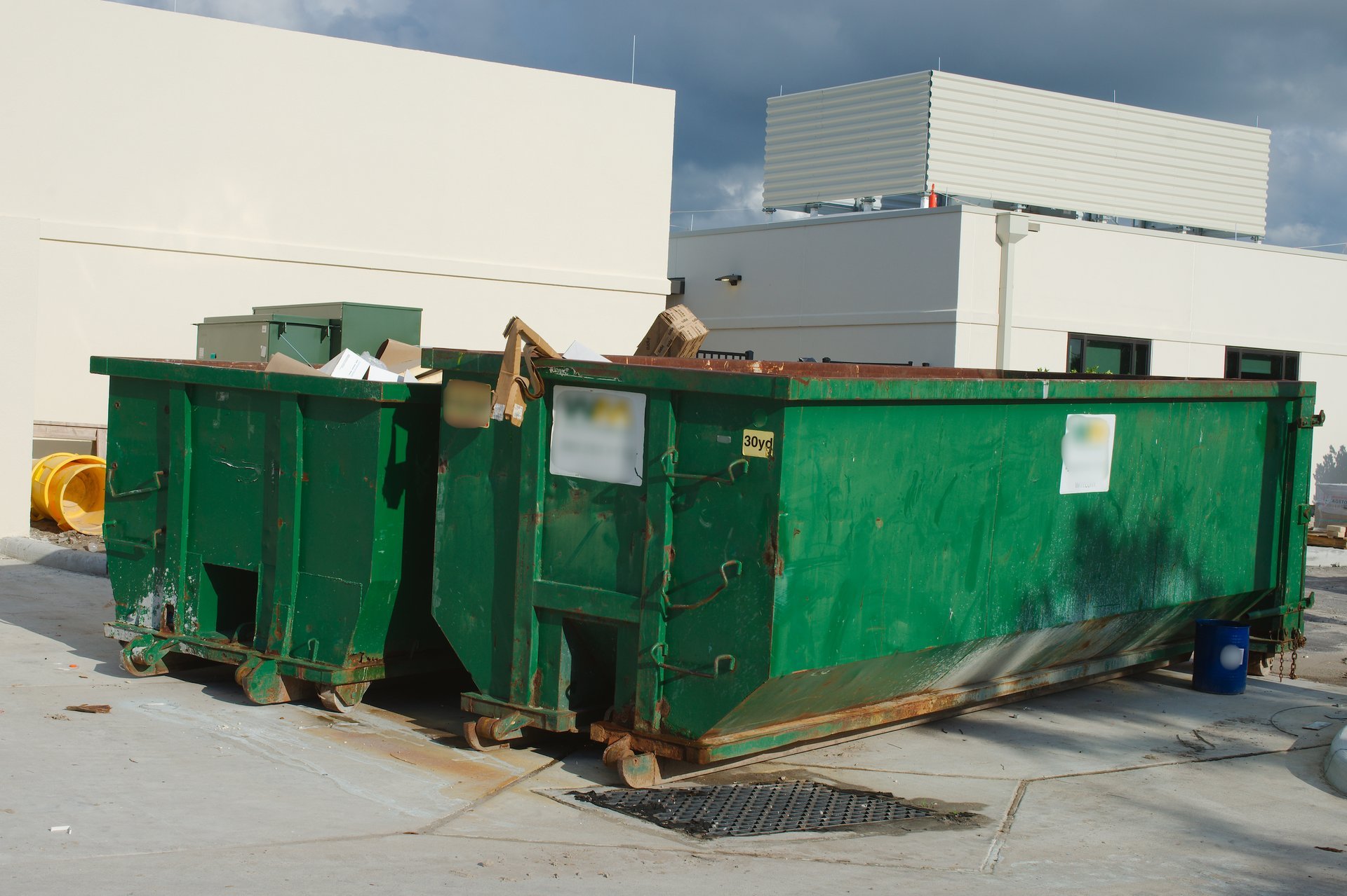 Large industrial dumpsters near white building exterior